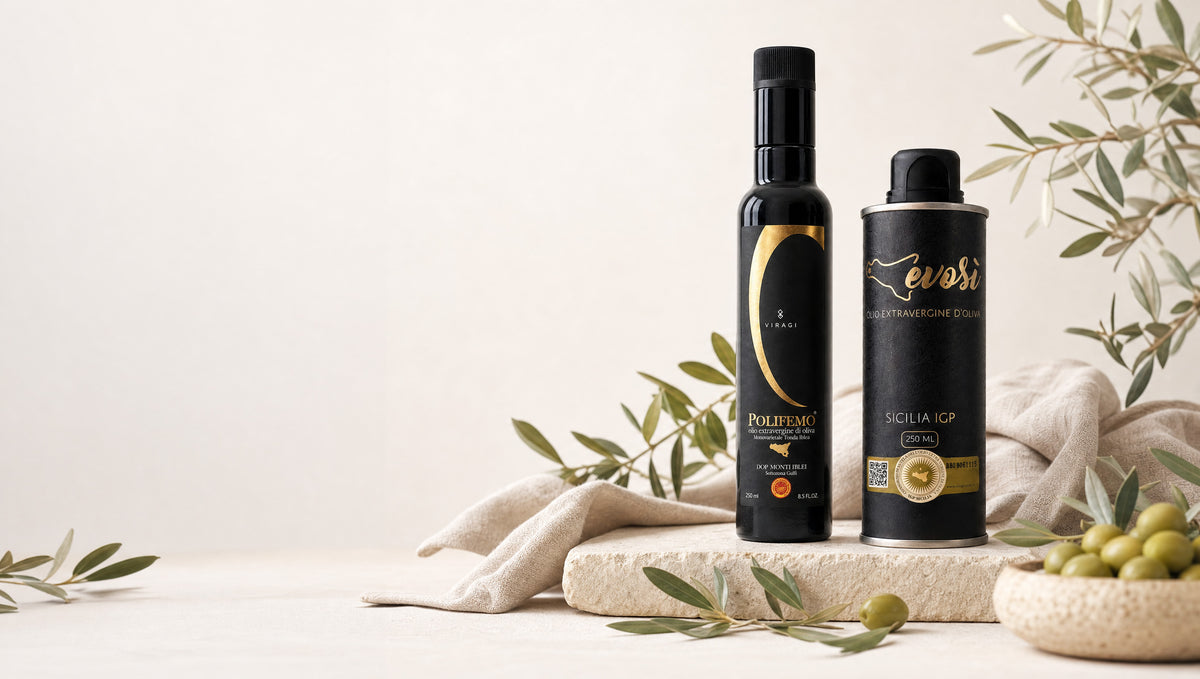 Two black bottles of Evosi and Polifemo olive oil stand on a stone slab with olive branches, green olives, and a beige cloth against a warm off-white background.
