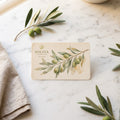 A Soliva Gift Cards gift card featuring an olive branch illustration, styled on a white marble surface with olive branches and a beige linen napkin.